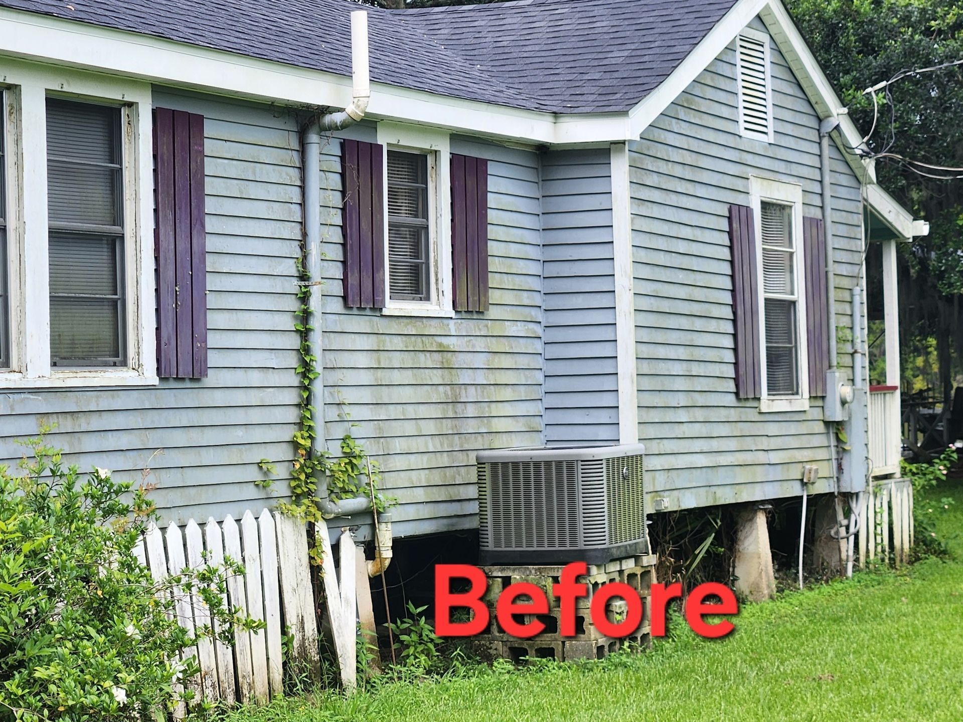 Side view of an old, weathered blue house with purple shutters and a visible air conditioning unit below the windows.