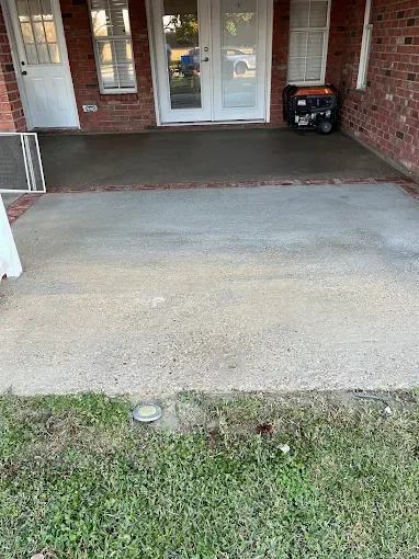 Concrete patio outside a brick building with French doors and a generator. The patio has a brick border and leads to a grassy area.