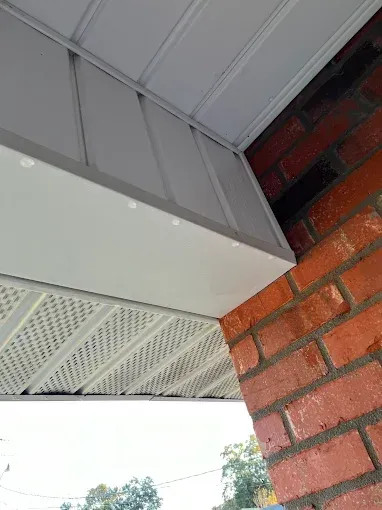 Low-angle view of white soffit and siding against red brick. The soffit has a vented pattern and is attached to the building's corner.
