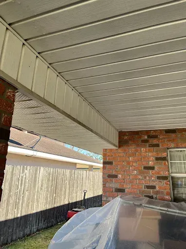 Under a covered patio, view of a white paneled ceiling and brick walls. A wooden fence and yard are visible in the background.