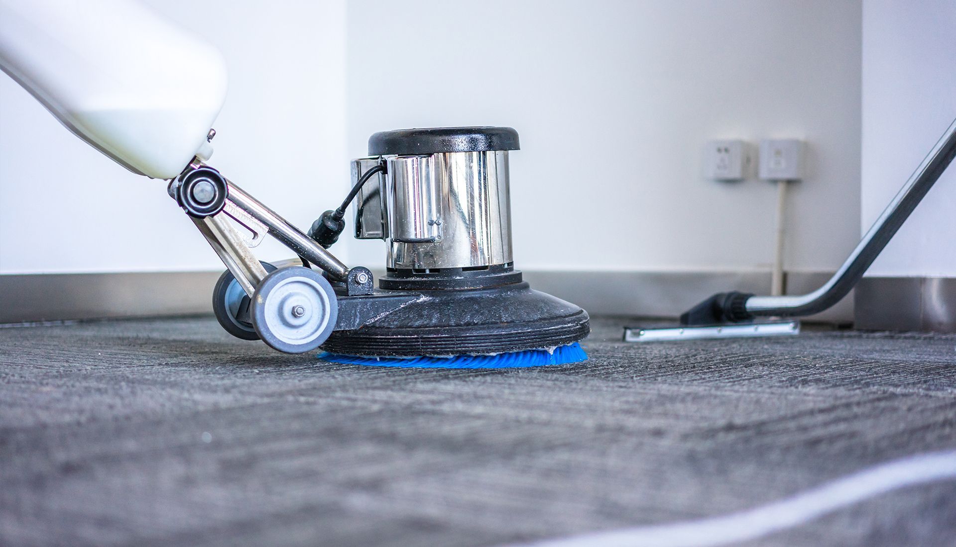 Floor cleaning machine scrubbing a gray carpet.