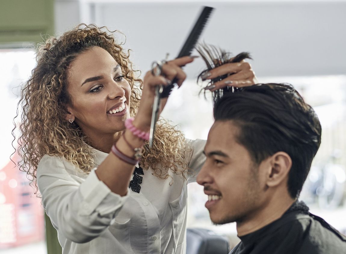 Close up of female barber cutting male customer's hair, both smiling.