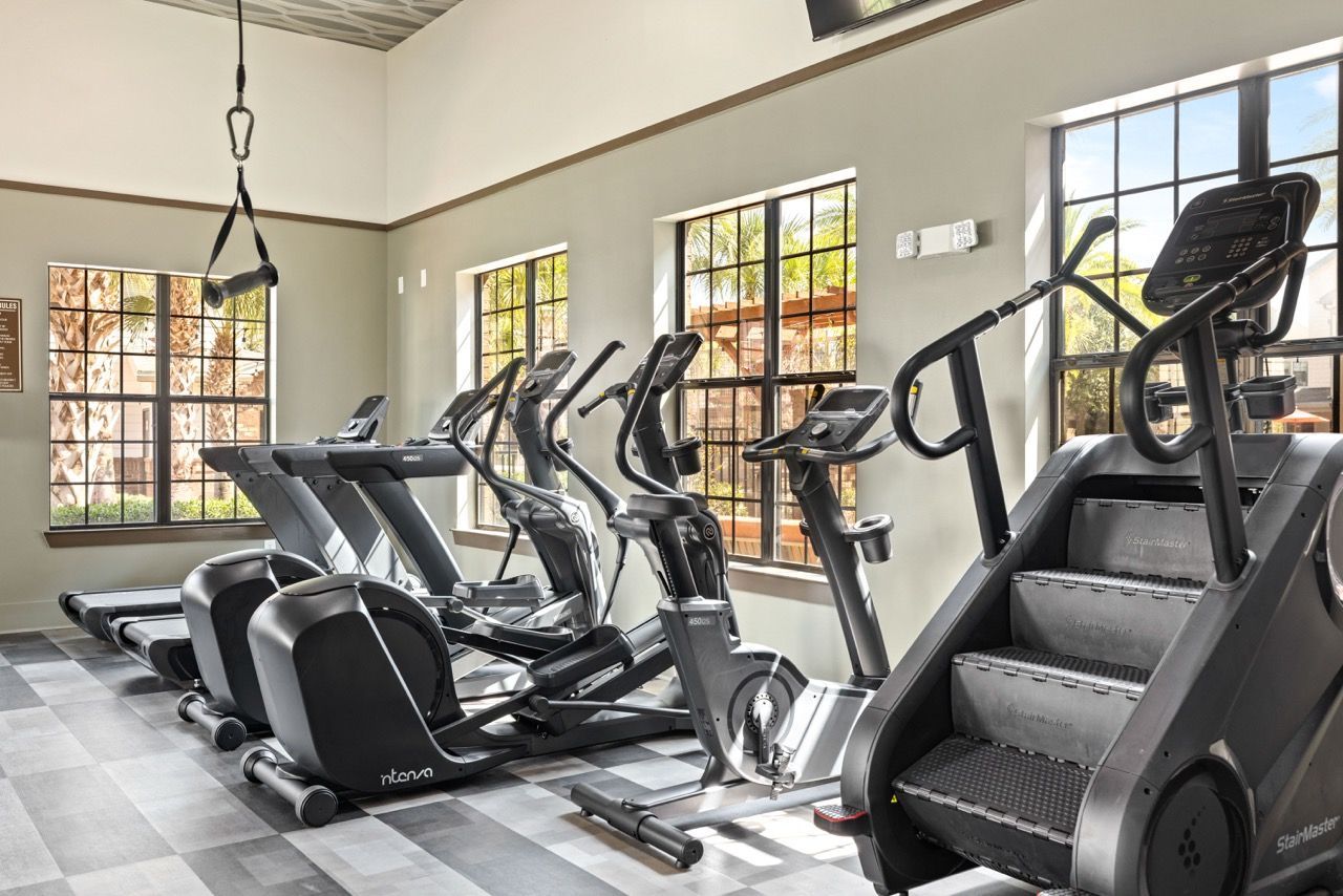 Indoor community gym with treadmills and elliptical machines by sunlit windows.