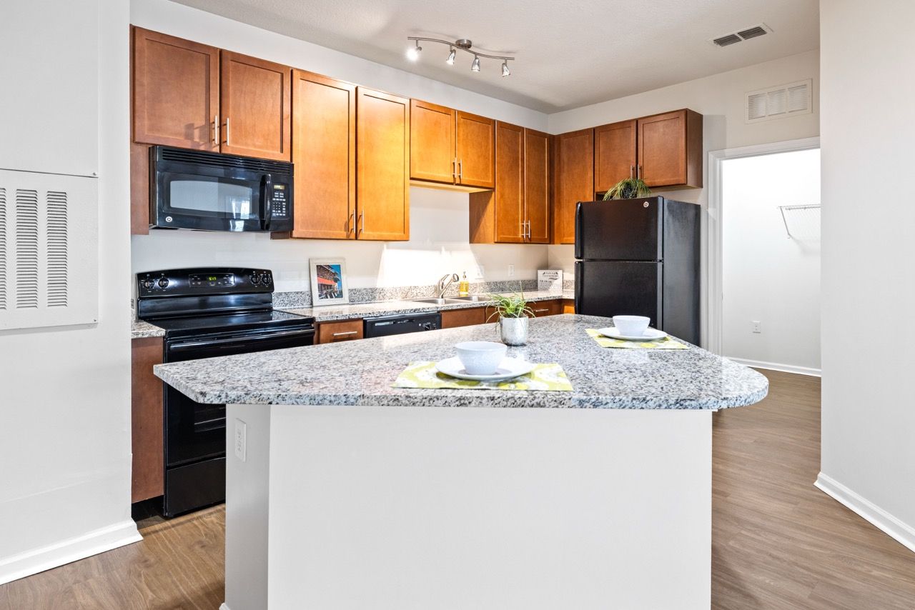 Kitchen in an apartment with granite countertops, wooden cabinets, and black appliances.
