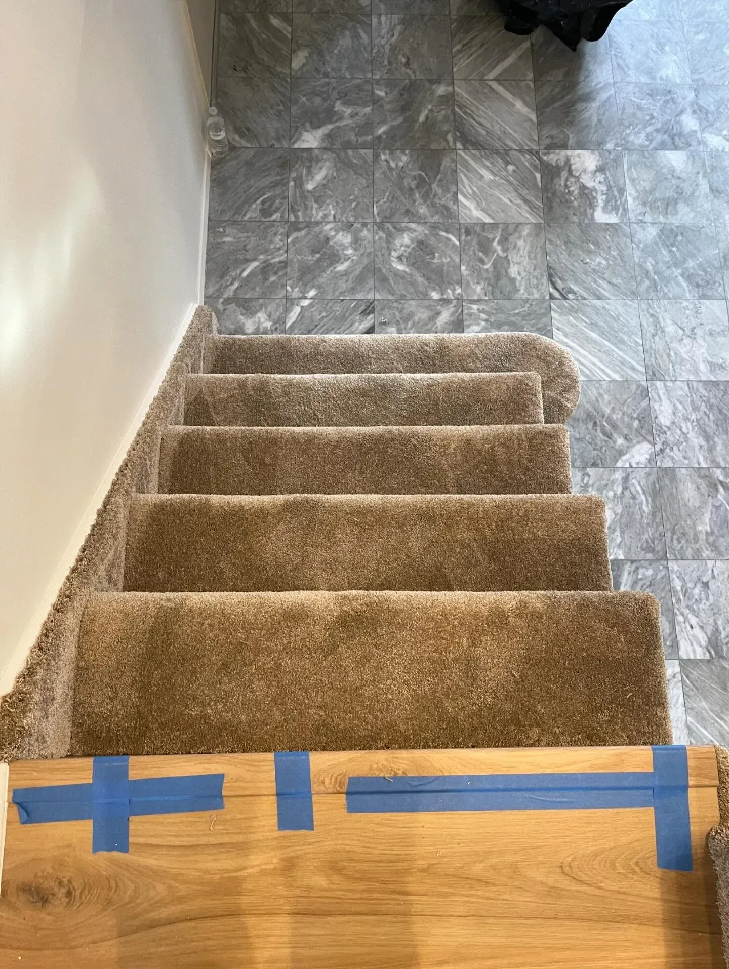 Carpeted stairs with blue tape marking the bottom step and a gray tiled landing above