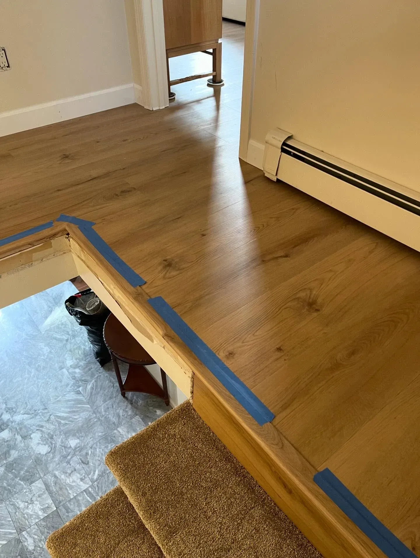 Wooden hallway with blue painter’s tape marking a step down to a carpeted stair opening