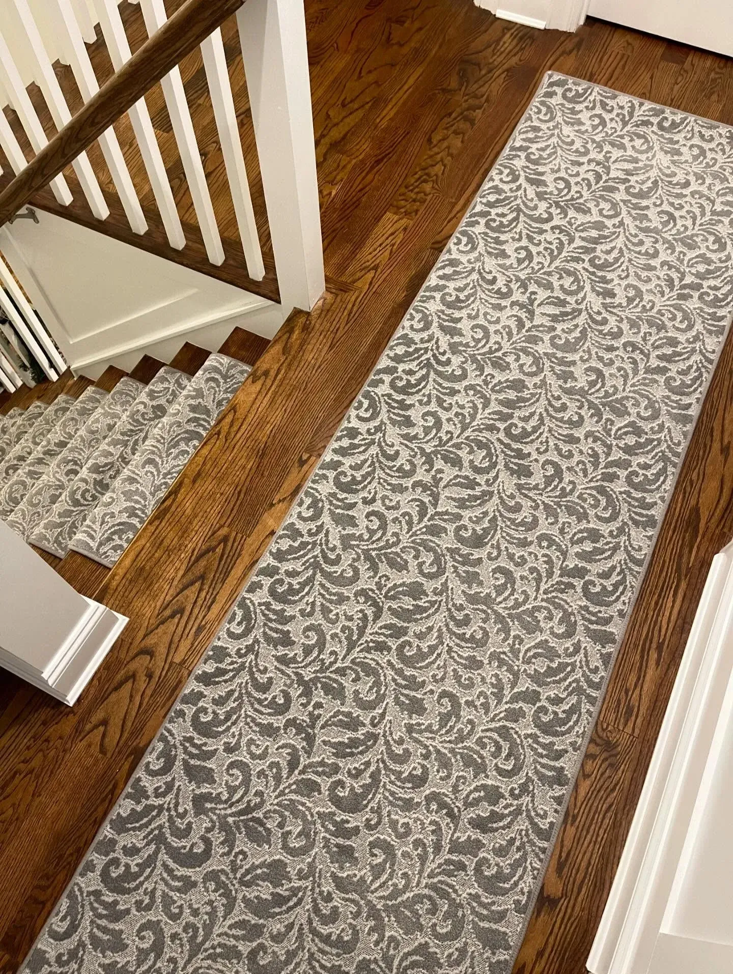 Narrow patterned runner rug on a hardwood hallway beside white stairs and trim.