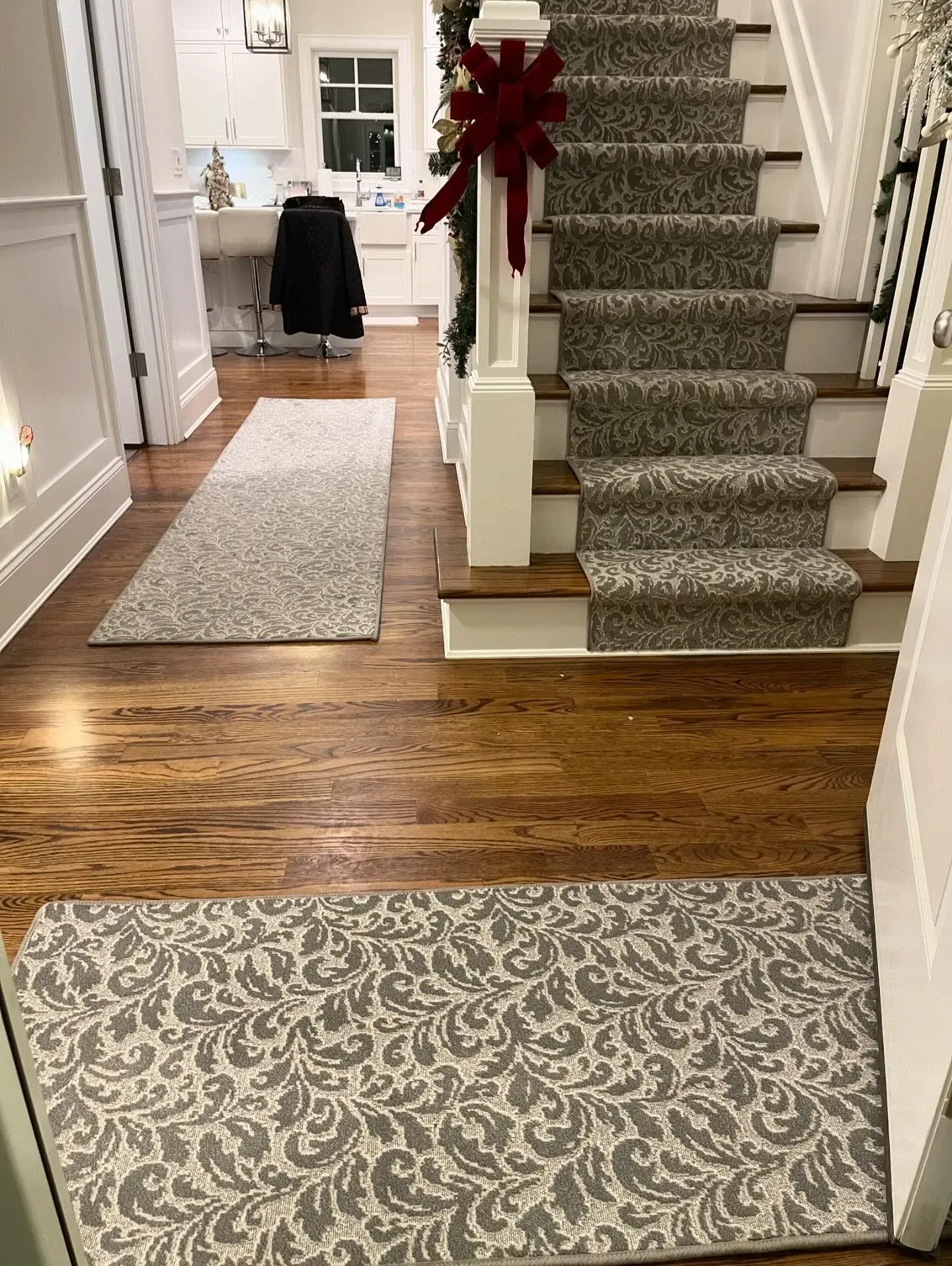 Hallway with staircase, patterned rugs, hardwood floor, and a large red bow on the banister