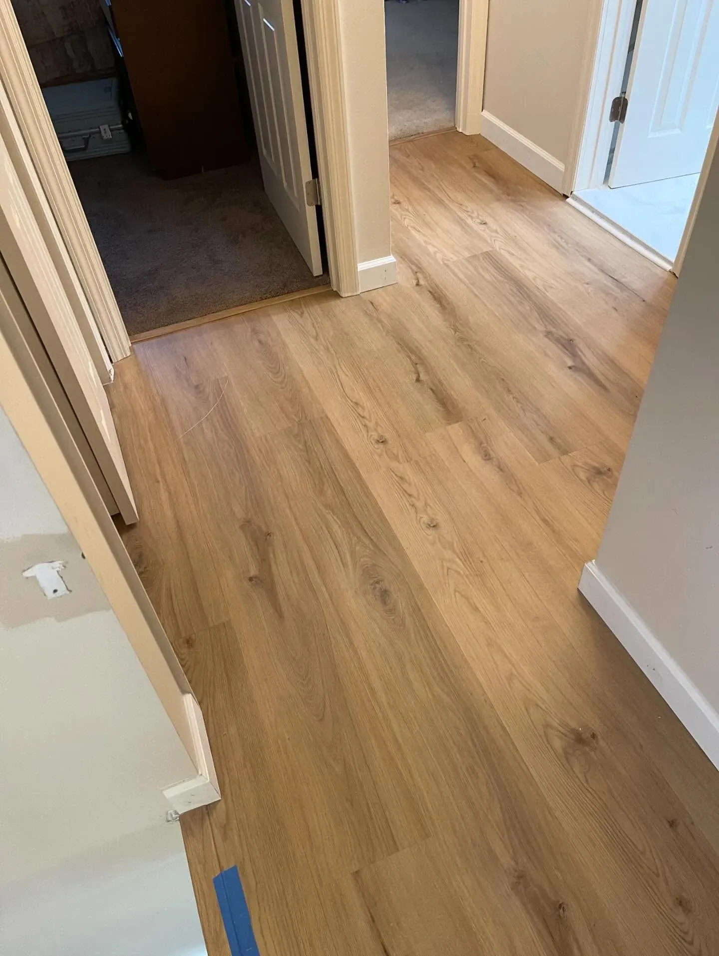Hallway with light wood flooring and white trim, leading to a doorway and adjacent rooms