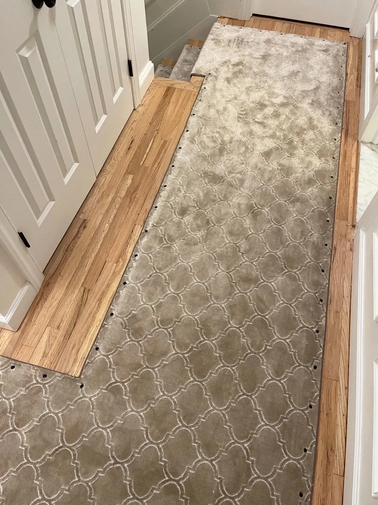 Narrow hallway with a gray patterned runner carpet and exposed wood flooring along the edges.