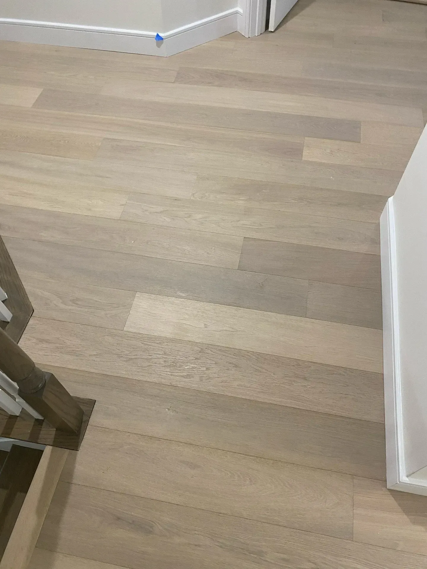Light wood flooring in a hallway with white baseboards and doorway trim