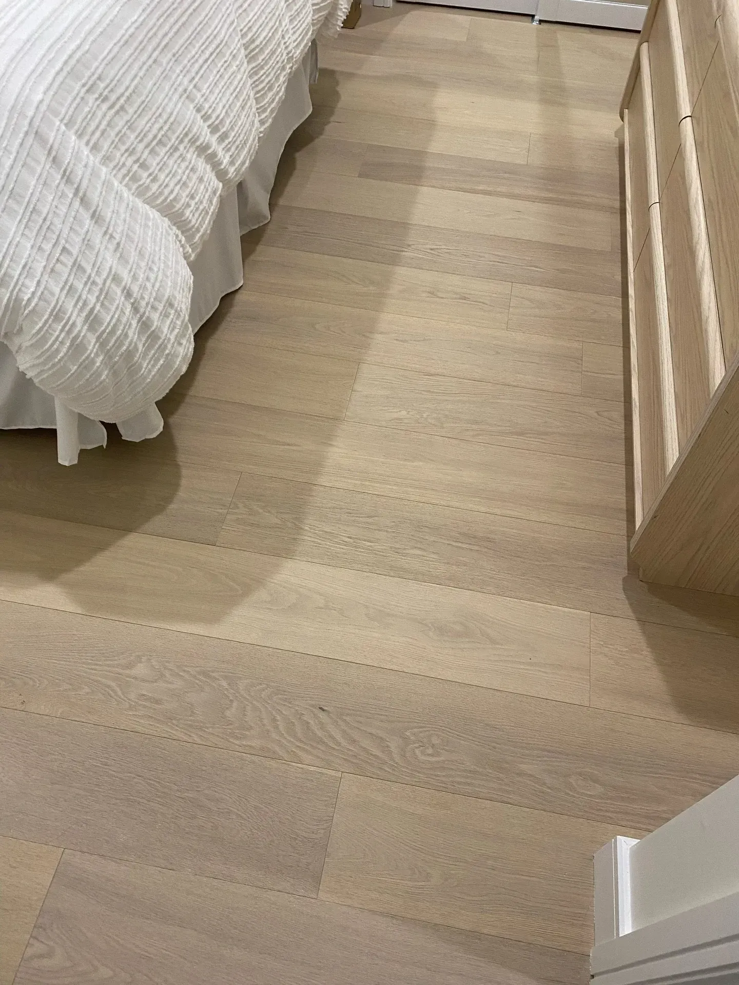 Wooden bedroom floor beside a bed with white bedding and a light wood dresser.