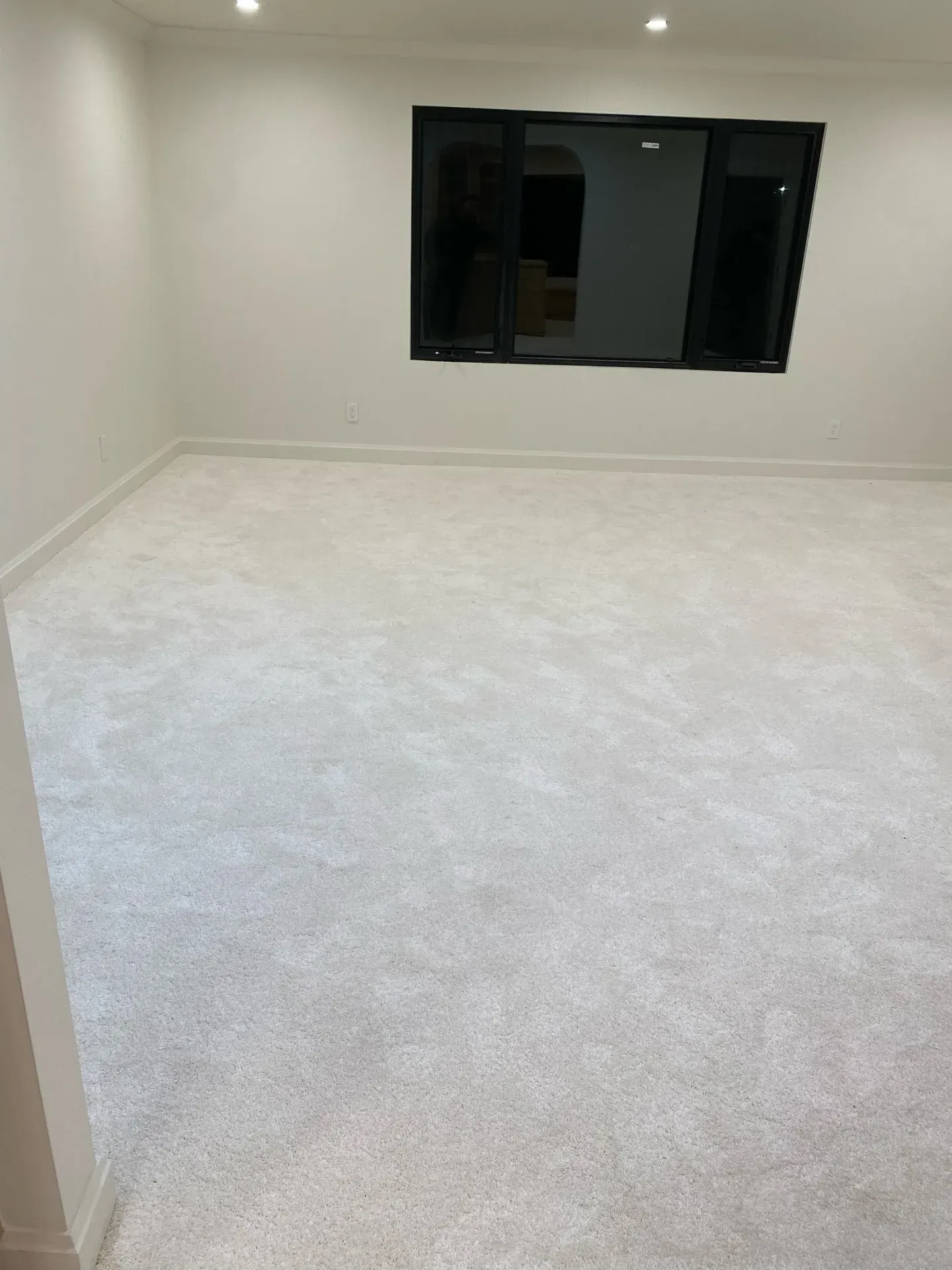 Empty white carpeted room with a dark window on the far wall