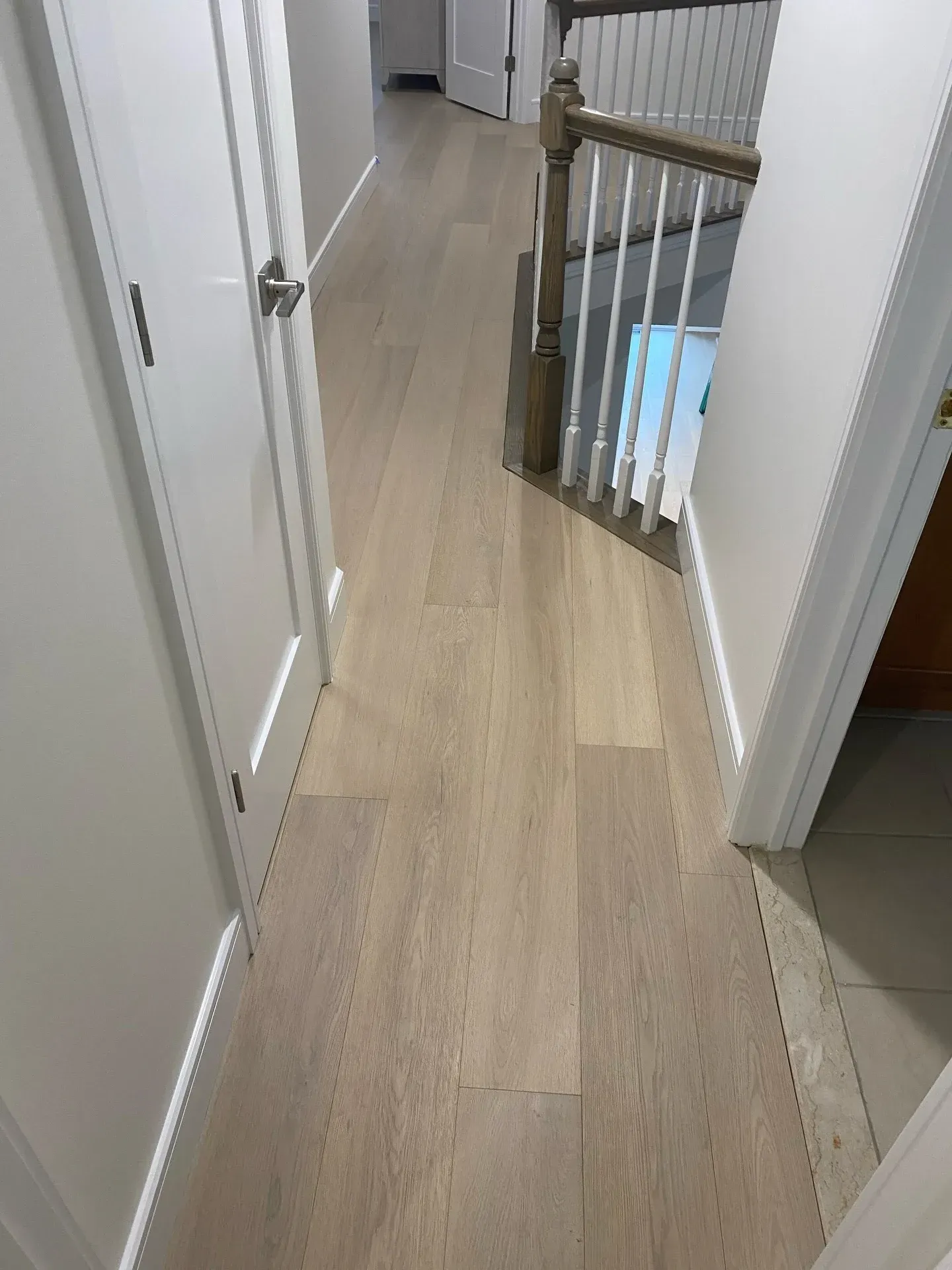 Narrow upstairs hallway with light wood floor, white walls, and a stair railing at the end.