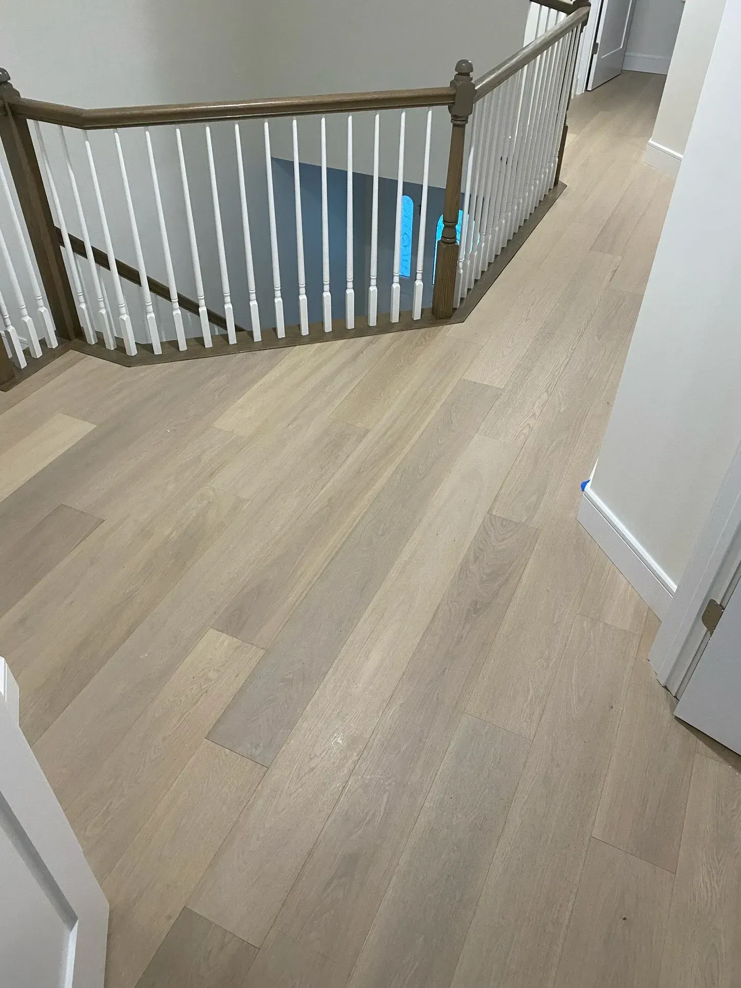 Hallway with light wood floors and a curved staircase railing overlooking the lower level