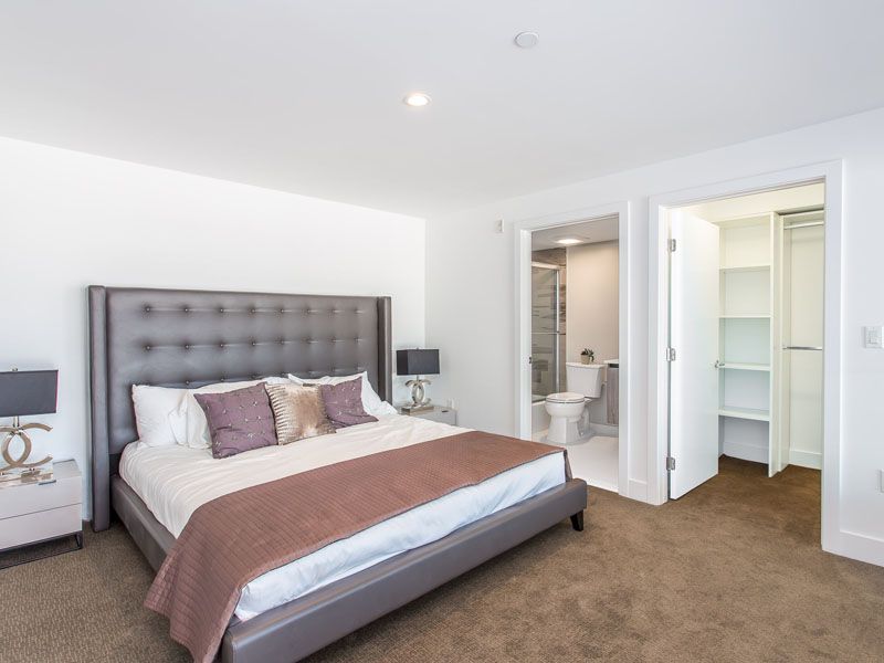 Bedroom with large bed, adjacent bathroom and closet; neutral colors, carpeted floor.