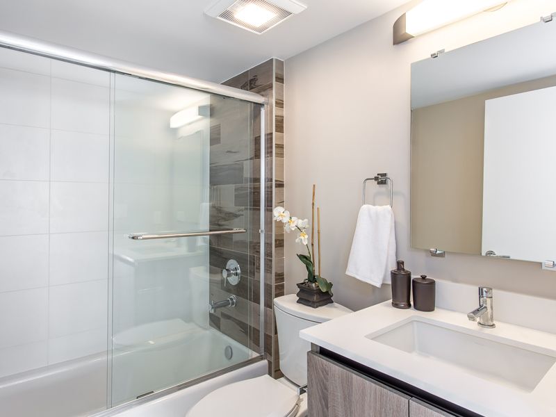 Bathroom with white tub, glass shower door, white sink, gray vanity, and neutral-colored walls.