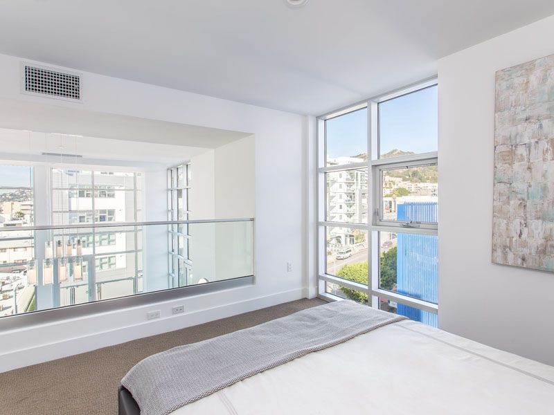 Bedroom with large windows, city view, white walls, and a bed with a gray blanket.