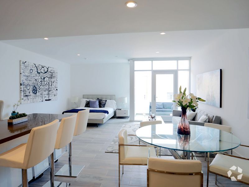 Bright, open-plan apartment with bedroom, dining, and living areas. White walls, modern furniture, and large windows.