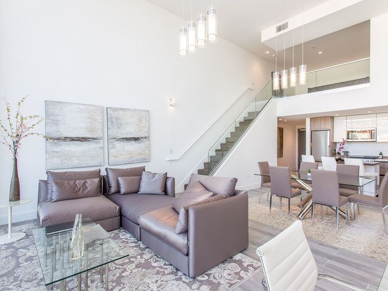 Modern living room with sectional sofa, glass table, dining area, and staircase.