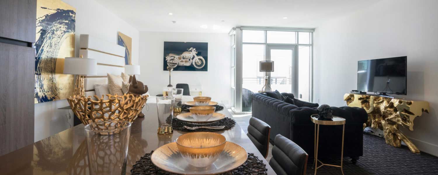 Modern apartment interior with gold and black accents. Dining table set with decorative plates and a living room with a sofa.