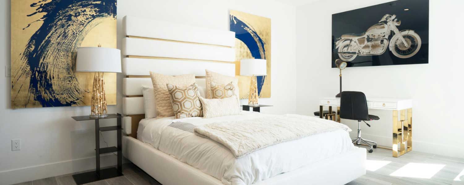 A modern bedroom with a bed, artwork, a desk, and gold accents.