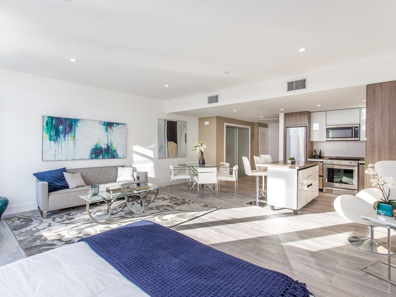 Modern open-concept living space with a kitchen, dining area, and living room. Neutral tones and large windows.