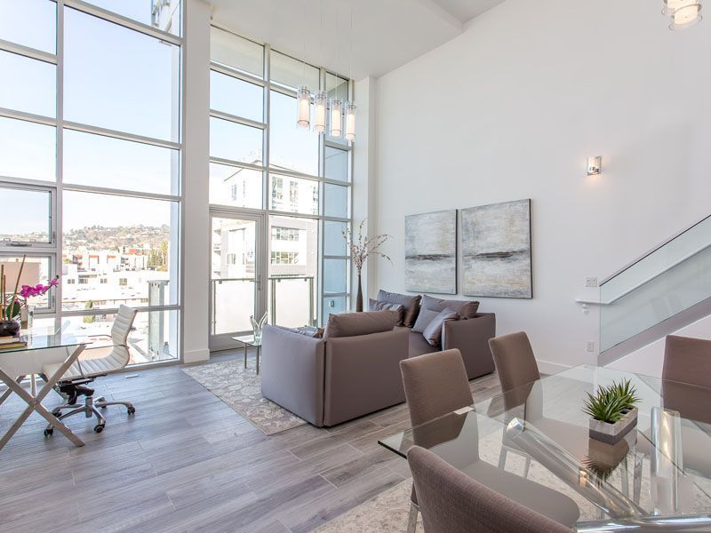 Spacious modern living room with large windows, gray furniture, and dining area.