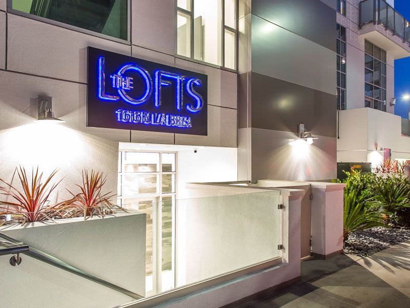 The Lofts apartment building entrance with a neon sign, lit pathway, and landscaping.