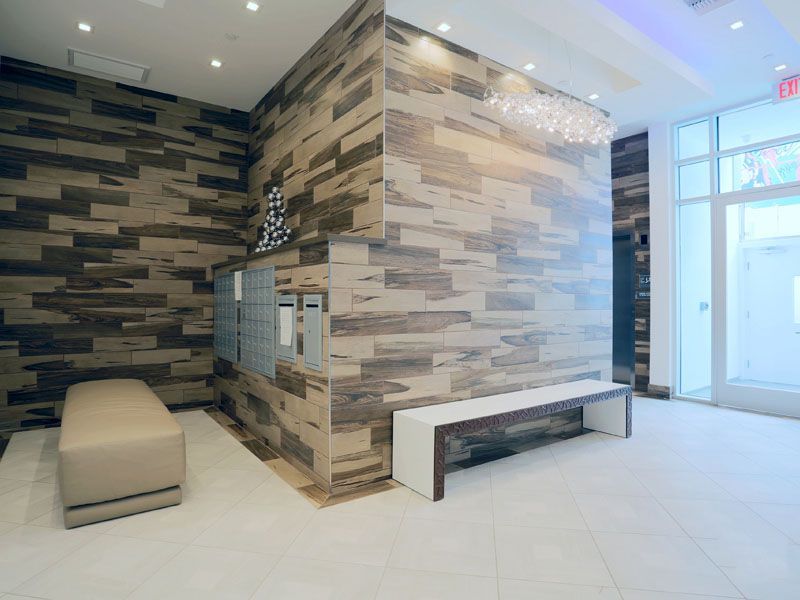 Modern lobby with wood-look tile walls, white flooring, bench, mailboxes, and a bright chandelier.