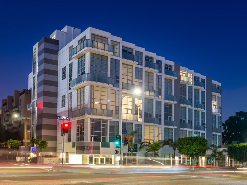 Modern multi-story building at dusk with illuminated windows and street traffic.