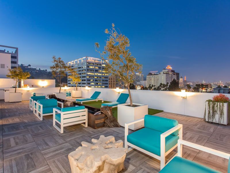 Rooftop patio with turquoise furniture, artificial turf, and city view at dusk.