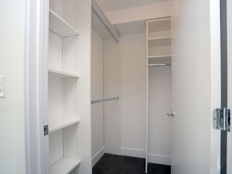 Empty white closet with built-in shelves and a clothing rod. Door on the right.