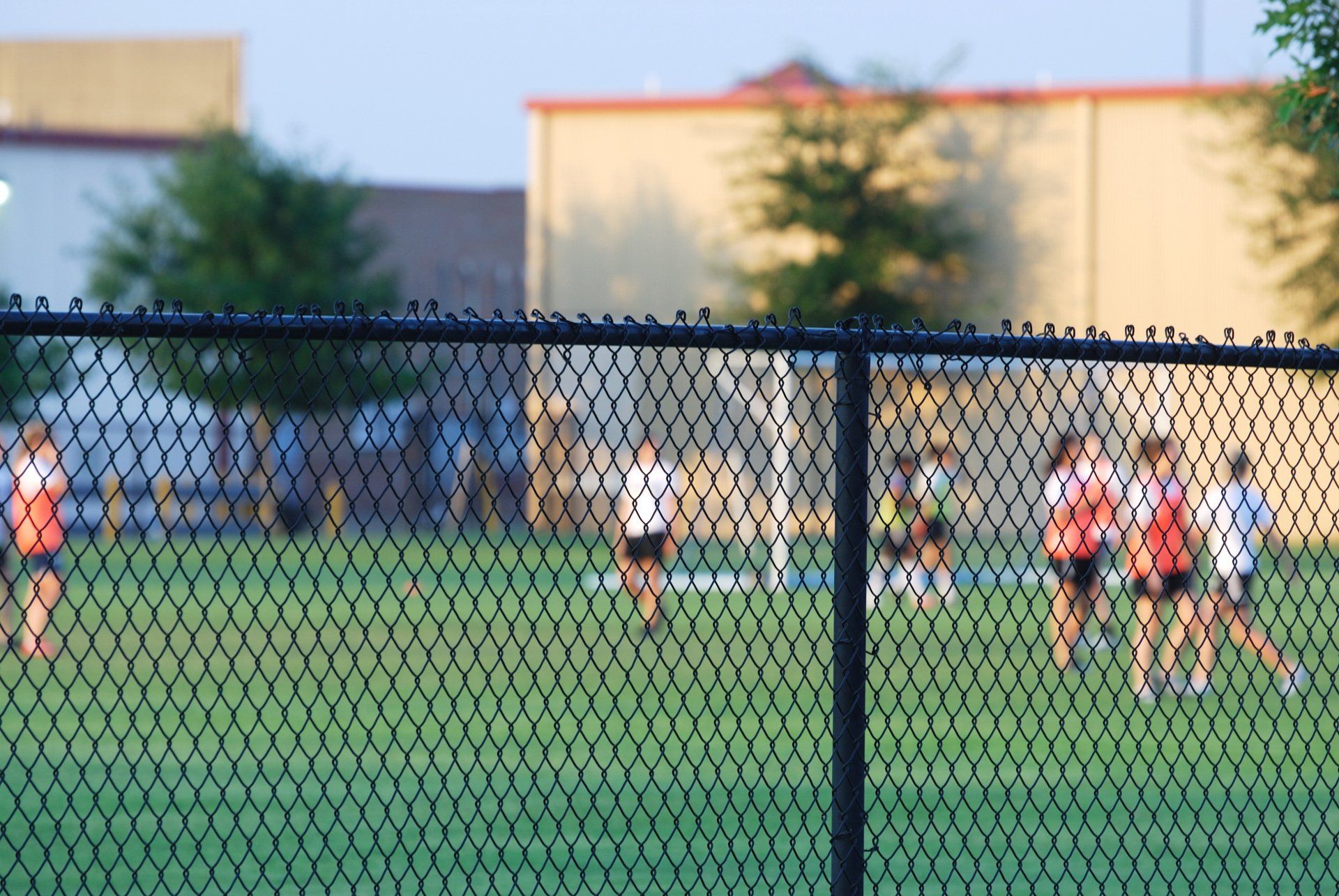 chain link fencing with soccer players in the field behind