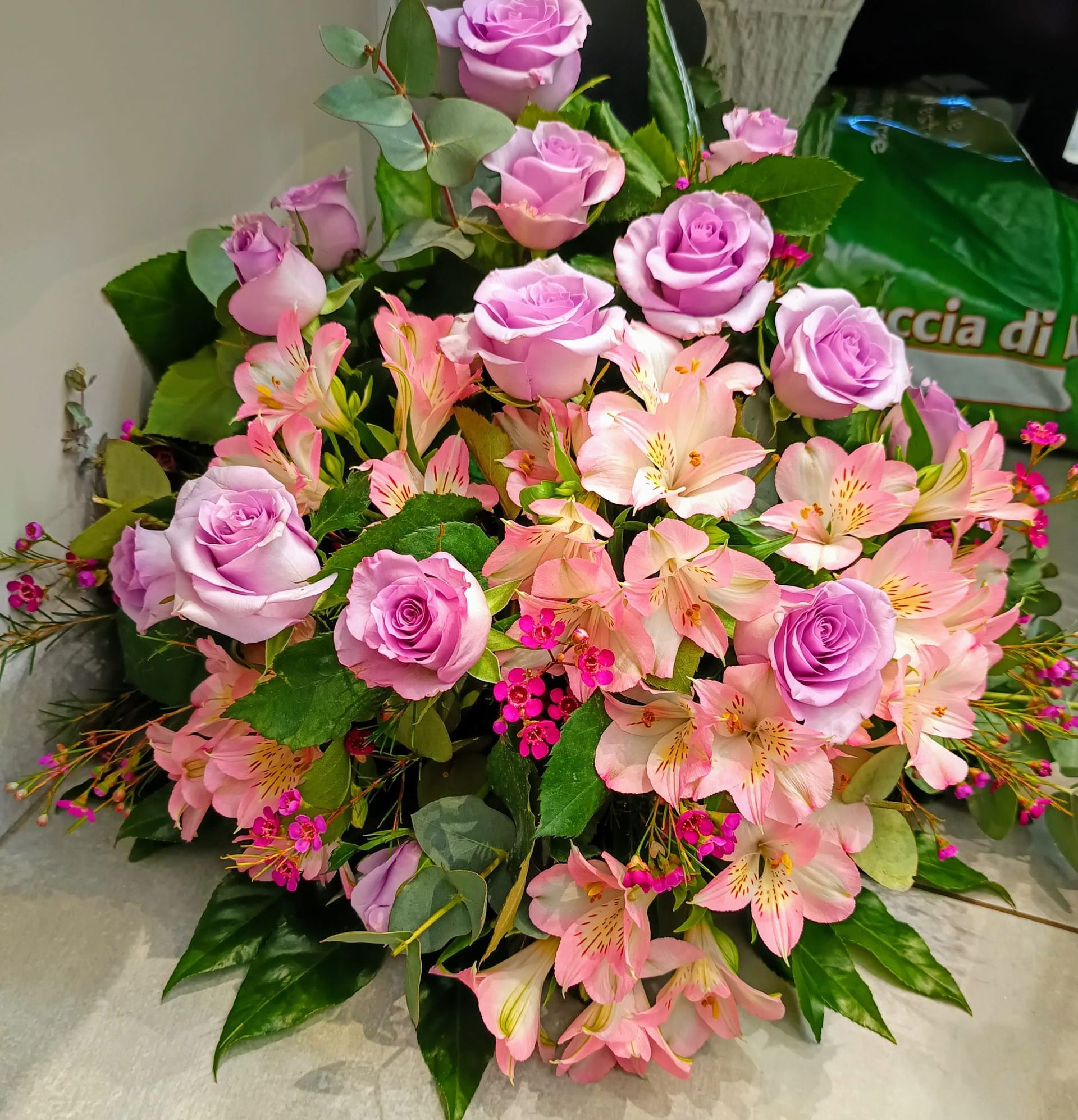 Un mazzo di fiori rosa con una borsa verde con scritto ccia di sopra