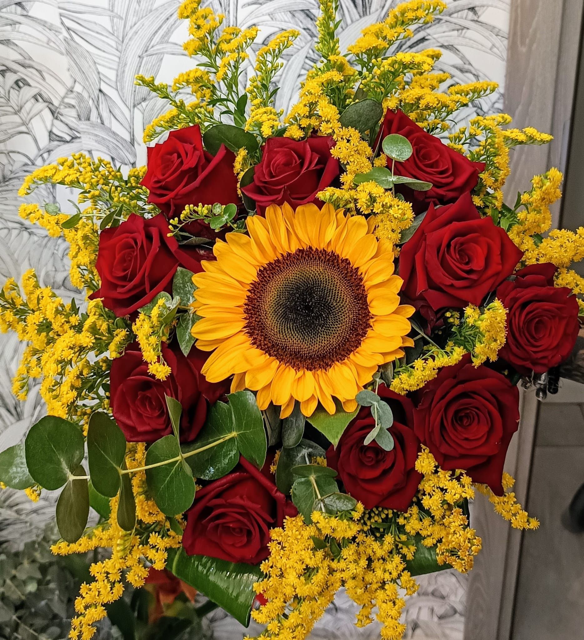 Un mazzo di rose rosse e fiori gialli con un girasole al centro