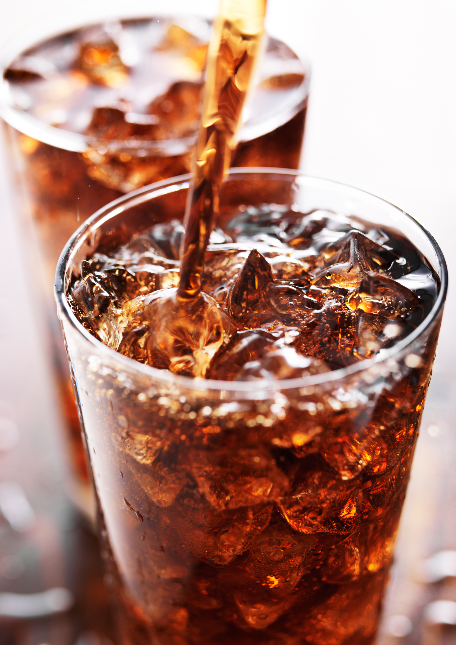 Two glasses of cola with ice are being poured into each other