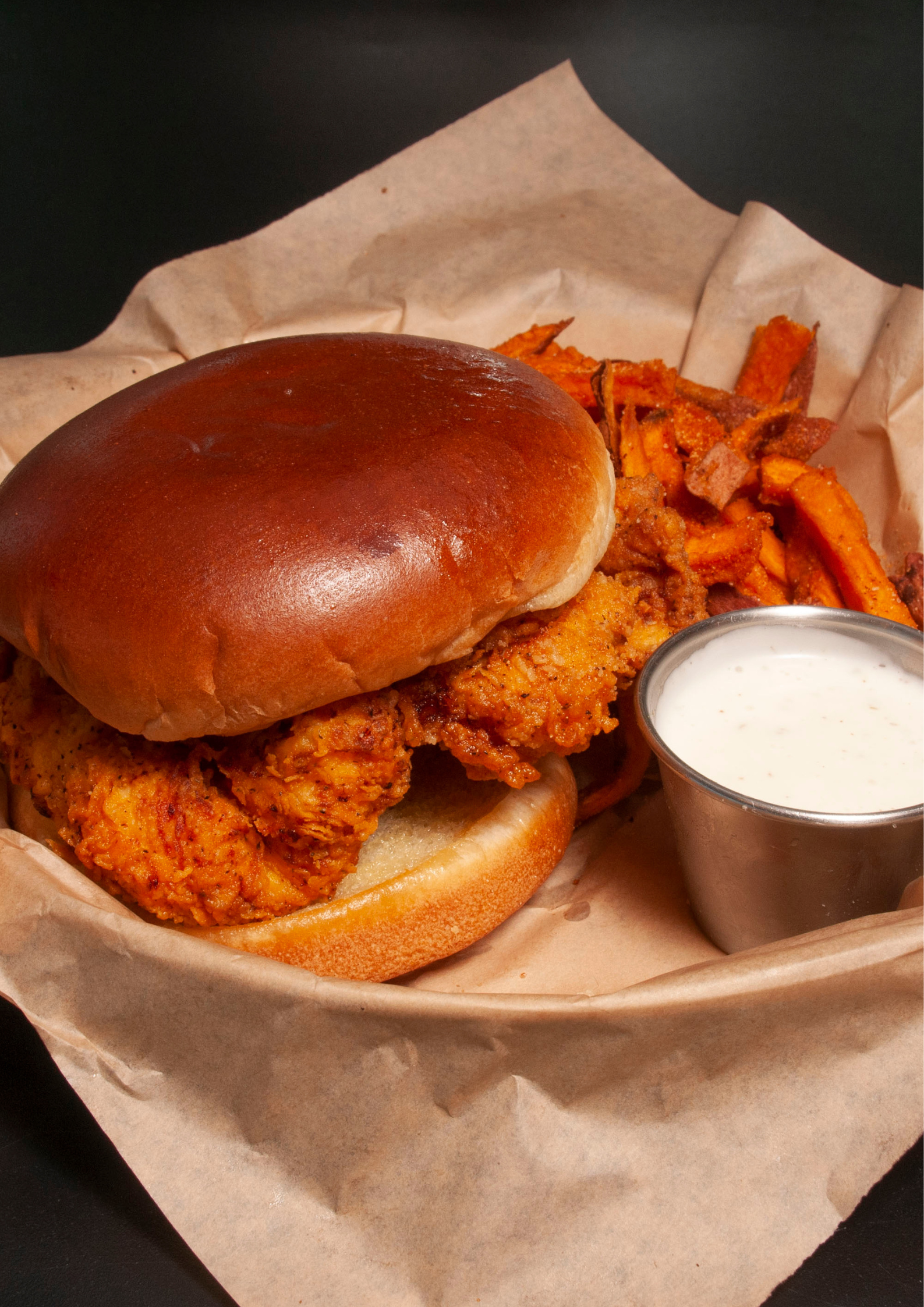 A chicken sandwich with sweet potato fries and ranch dressing in a basket.