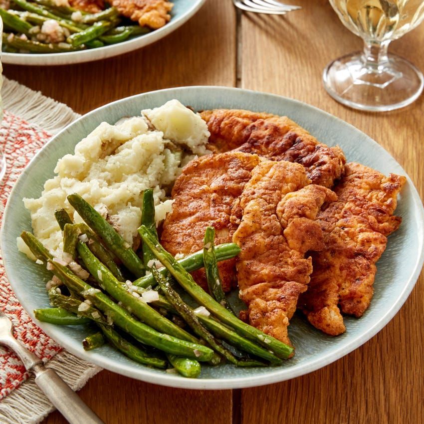 A plate of food with mashed potatoes green beans and chicken on a table.