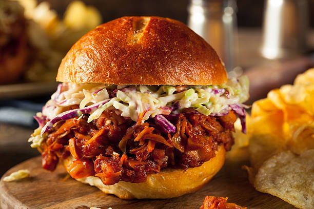 A pulled pork sandwich with coleslaw and chips on a wooden cutting board.