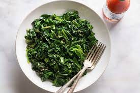 A bowl of spinach with two forks next to a bottle of tomato sauce.