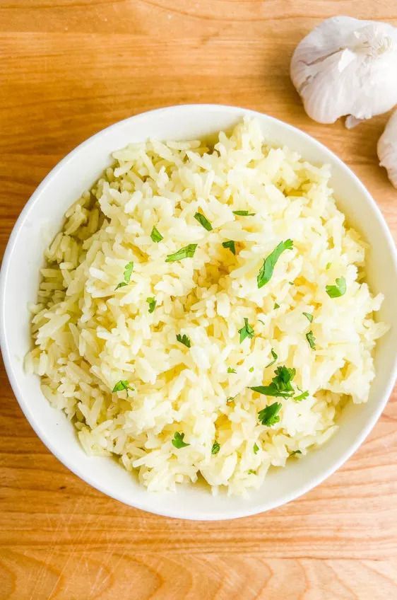 A bowl of rice with garlic and parsley on a wooden table.