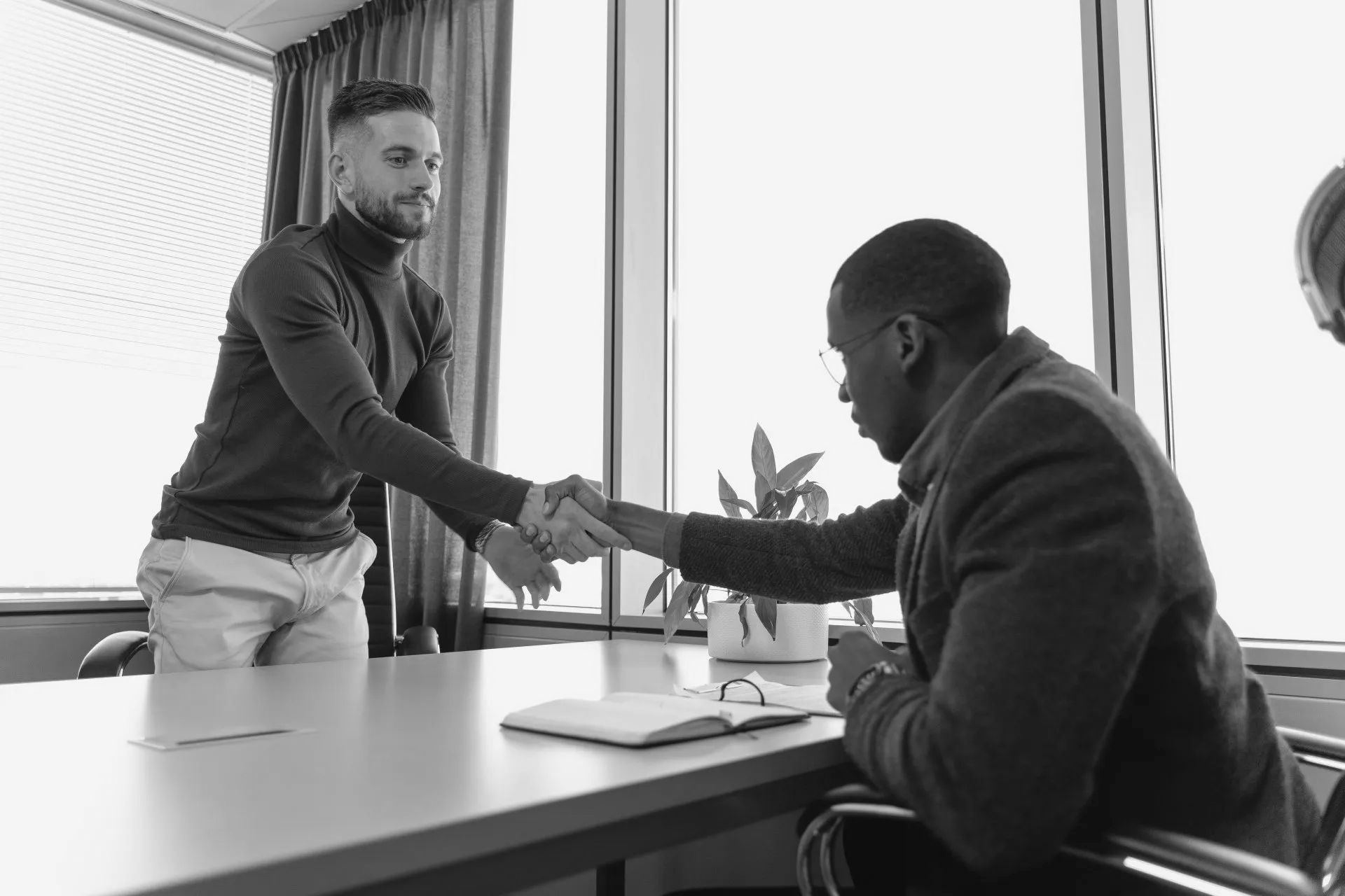 Two men are shaking hands while sitting at a table.