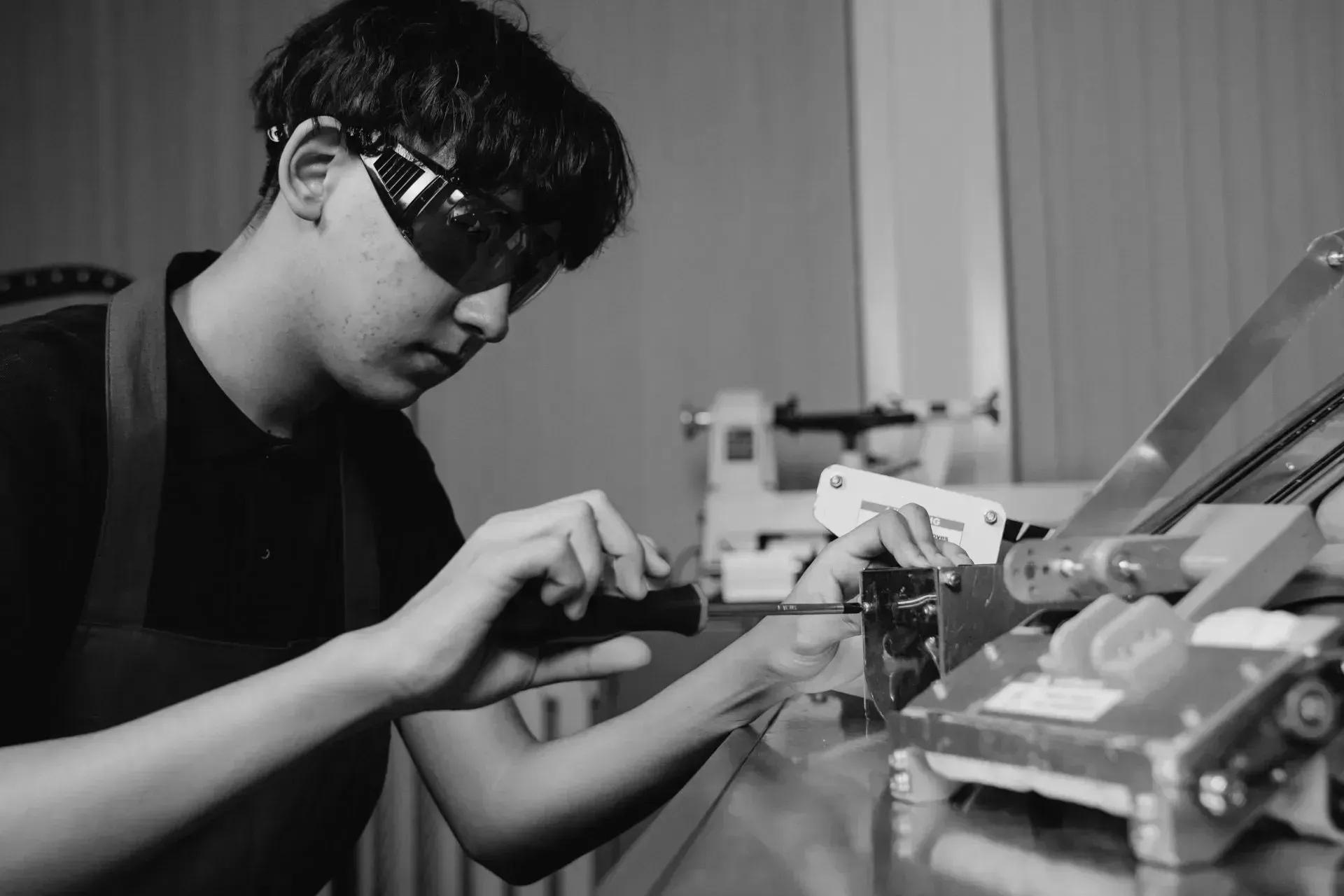 A man wearing safety glasses is working on a machine in a factory.