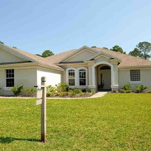 Single-story cream house with a front lawn and blue sky