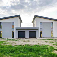 Modern white duplex house with two black garage doors and a grassy front yard