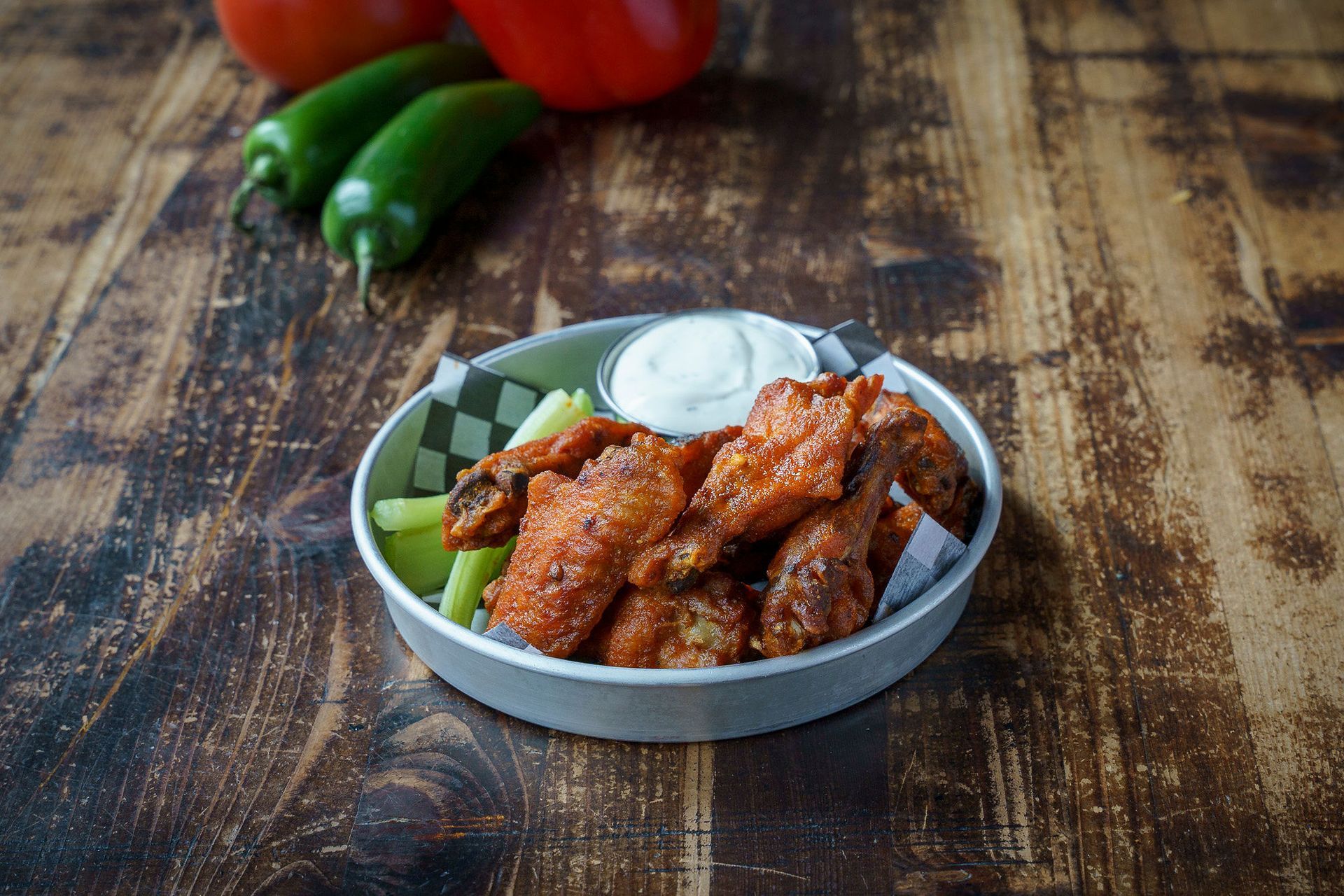 Buffalo wings with ranch, celery, and jalapeños on a wooden table.