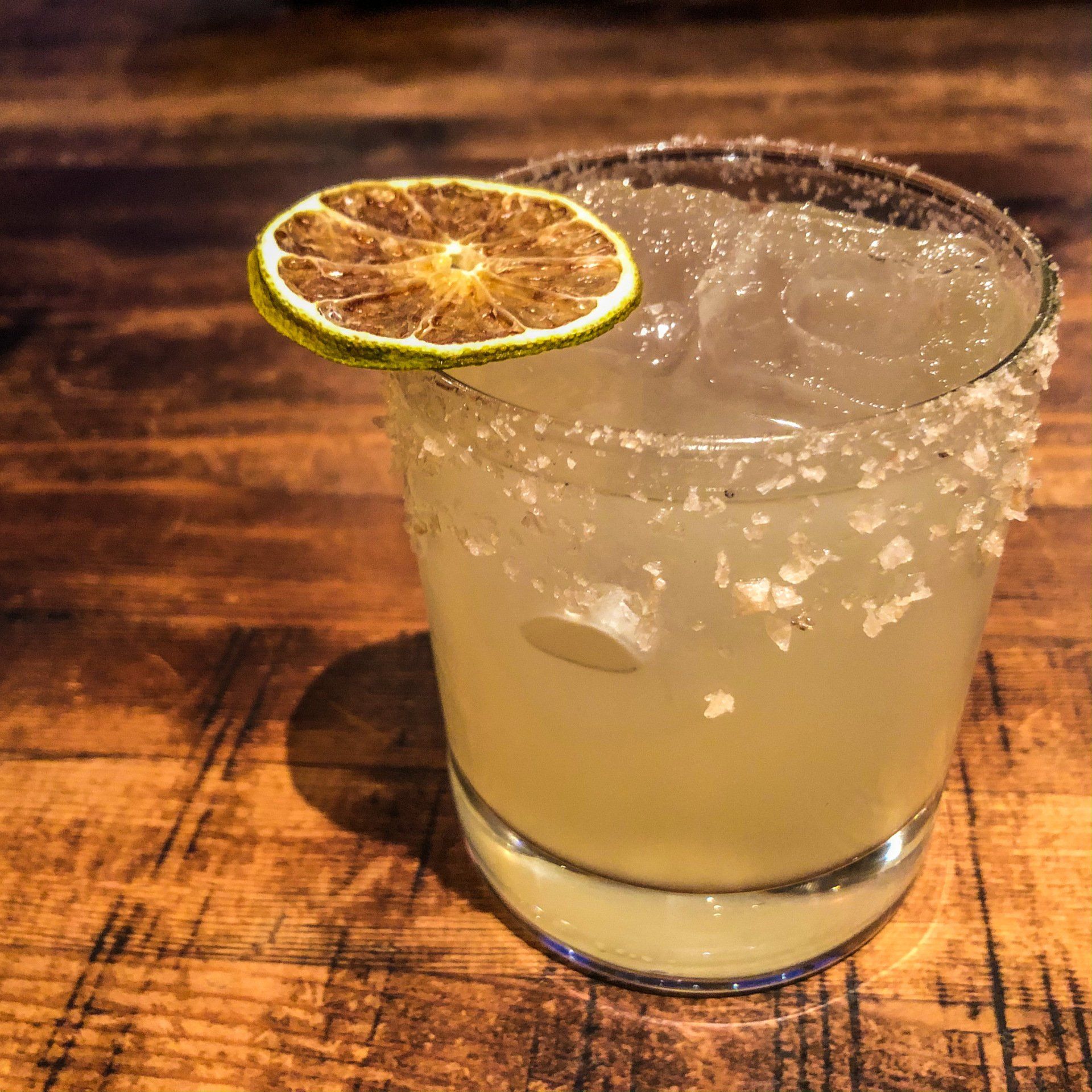 Margarita in a salt-rimmed glass with a dried lime slice garnish on a wooden table.