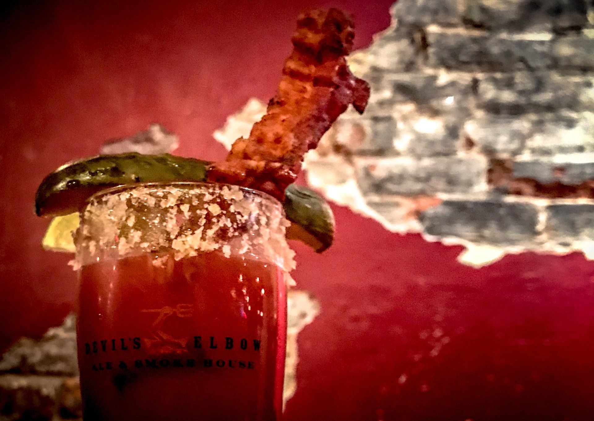 Bloody Mary cocktail with bacon, lime, and a salt-rimmed glass, set against a brick wall.