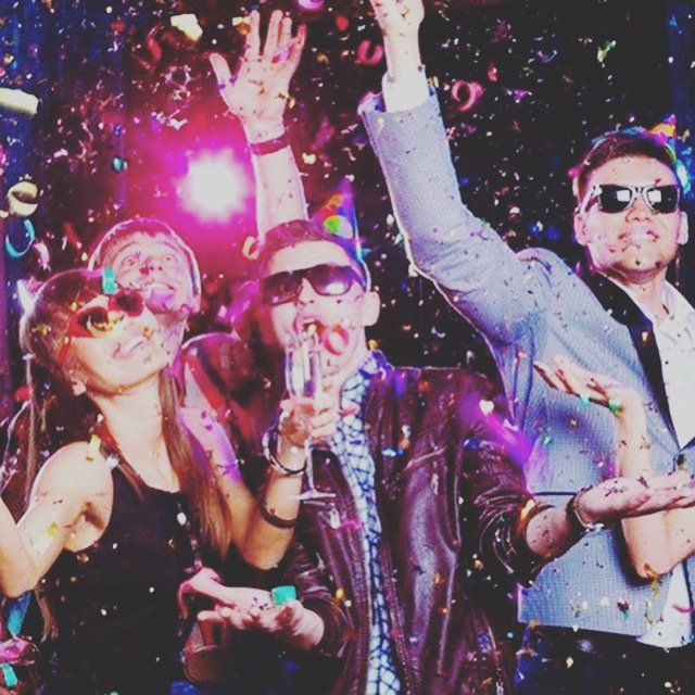 People celebrating at a party with confetti, champagne, and sunglasses, indoors, excited.